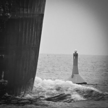 The snowy owl watches as the ship passes her on the buoy in Lake Huron. The ship industry impacts the water, air and species that are subjected to noise pollution, air pollution and discharge.