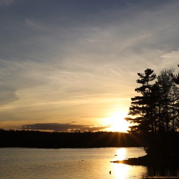 The sun falls over the horizon, disappearing behind the trees at West Lake, NS.