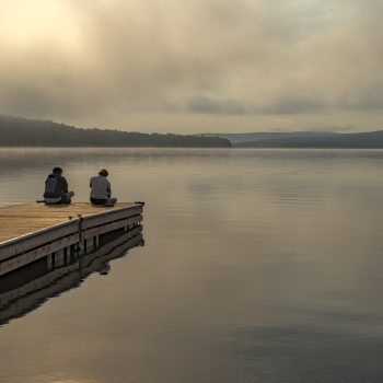 Deux personnes au lever du soleil sur un grand lac brumeux et calme, quelque part en Mauricie.