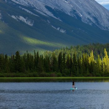 This was taken in the golden hour at Vermillion Lakes 2. The paddle boarder traversed the entire lake, enjoying the lakes stillness and the approaching sunset light.The water was a deep blue, the clou ...